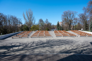 view from the stage to empty benches for spectators in a city park. A row of wooden benches in an...