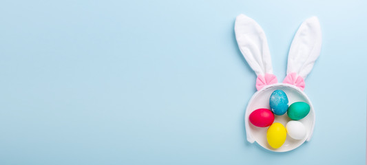 Cute Easter composition. Multicolored easter eggs and bunny ears on blue background. Top view. Copy space