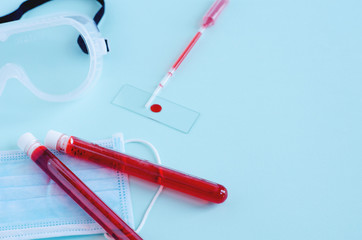 Test tubes with red liquid close-up lie on a disposable mask. Nearby lies a glass for clinical blood analysis with a drop and a pipette. Horizontal background.