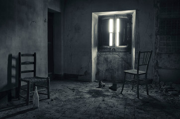 Habitación de casa abandonada con sillas iluminadas en la penumbra por una ventana.
