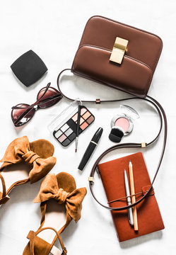Cross body brown leather bag, suede wedge sandals, cosmetics, sunglasses on a light background, top view. Fashion concept