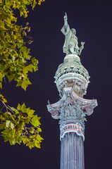 Fototapeta premium Estatua de colon de Barcelona por la noche con hojas de árbol.