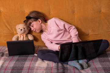 A school kid is studying on a laptop while sitting on a sofa.