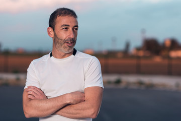 Caucasian athlete man with white t-shirt, looking to the side with serious face, posing on the street with a blue sky of clouds