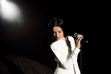 Portret of a singer with mic in hand singing popular song on stage in white lights.