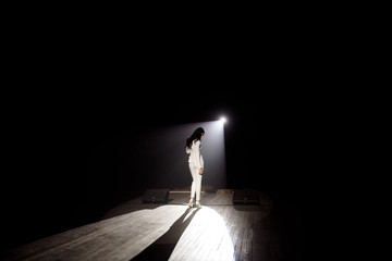 Back view of a singer with microphone singing a song on stage in white lights.