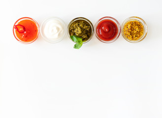 Sweet chili sauce, mayonnaise, pesto, ketchup and french mustard and in glass bowls and spoons on a...