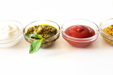 Close-up various sauce and dip with selective focus on white background. Mayonnaise, pesto, ketchup and french mustard in glass bowls