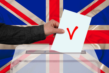 male voter drops a ballot in a transparent ballot box against the backdrop of the Great Britain...