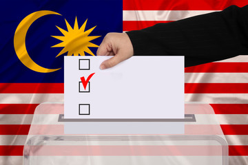 female voter drops a ballot in a transparent ballot box against the background of the Malaysia national flag, concept of state elections, referendum