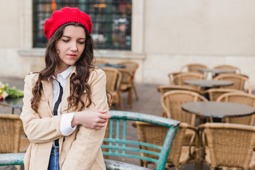 Beautiful young woman wearing red beret at city street of European city. Happy tourist girl walking outdoors. Spring portrait of pretty brunette female posing in old town.