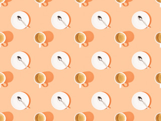 top view of cups of fresh coffee and spoons on plates on orange, seamless background pattern