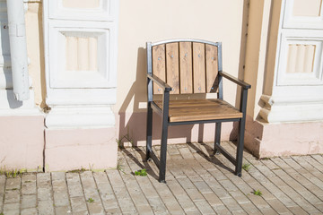Fototapeta na wymiar wooden chair on the sidewalk near the wall of an old house, lit by the sun