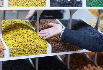 A girl seller in the market offers customers various dried fruits and nuts.