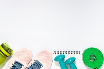 Healthy lifestyle and fitness concept. Sport shoes, dumbbells, resistance band,water bottle and notepad on white background top view.