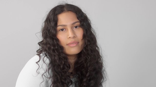 Mixed race plus size woman without makeup in studio watching to the camera and touch her face