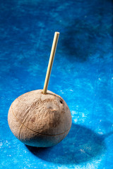 Fresh coconut with bamboo straw inserted in it on blue background. Zero waste and no plastic.