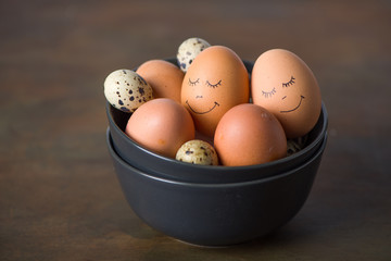 Natural eggs in dark bowls with hand painted faces. Easter concept