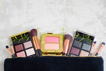 premium makeup brushes, blush pads and palette eye shadow in black cosmetic bag on a light marble background, creative cosmetics flat lay