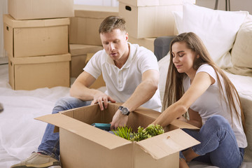 Portrait of happy couple looking at laptop computer together sitting in new house, surrounded with boxes