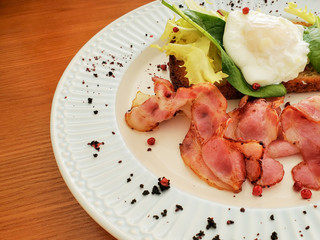 Freshly prepared Breakfast poached egg, toast and bacon with lettuce leaves. Breakfast plate on the table.