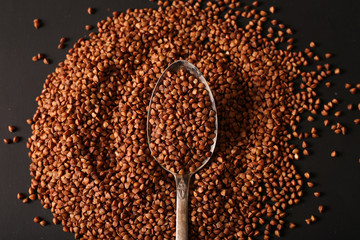 Handful of buckwheat in an iron spoon on a dark background