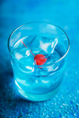 Blue old fashioned cocktail with cherry on the rustic background. Selective focus. Shallow depth of field.