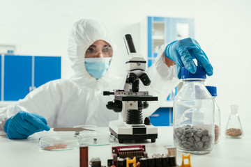 engineer in hazmat suit holding jar with gravel near microscope and computer motherboard