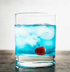 Blue old fashioned cocktail with cherry on the rustic background. Selective focus. Shallow depth of field.