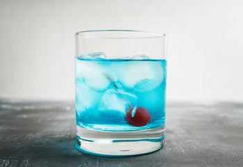 Blue old fashioned cocktail with cherry on the rustic background. Selective focus. Shallow depth of field.