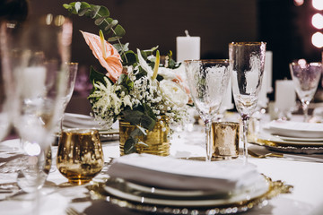 festive tables at the wedding party are decorated with flower arrangements, on the tables are plates with napkins and cards, glasses and candles