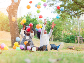 Two adorable African boy and girl laughing with happiness when colorful balls coming down to them.