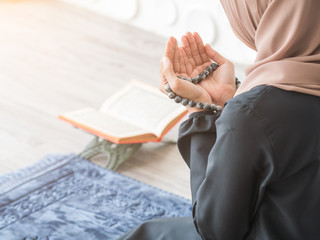 Selective focus on Moslem pray, praying hands with rosary beads of Muslim lady with blurry quran on table beside blue mat.
