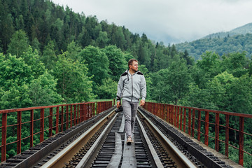 Fototapeta premium Young man on railway track on forest background