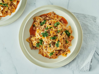 Pasta Farfalle with tomato sauce and ground meat in plate on white marble tabletop. Idea and recipes for easy, simple lunch or dinner one-pot meat goulash. Top down view or flat lay
