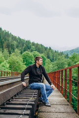 Fototapeta premium A man in jeans sits on a railway track. Railroad track on forest background.