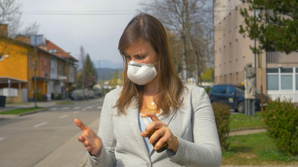 CLOSE UP: Young Caucasian businesswoman wearing a face mask sanitizes her hands.