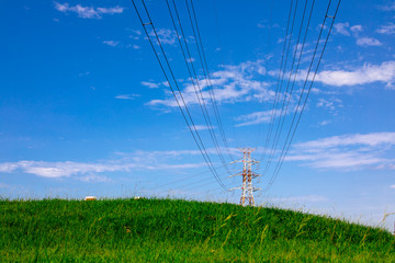 Electric tower on green grass in embankment park, city under blue sky and white clouds