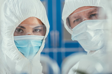 selective focus of biochemists in hazmat suites, medical masks and goggles looking at camera