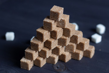 cane brown  sugar cubes in pyramid on black wooden background and white pieces