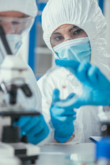 selective focus of biochemist shhowing petri dish to colleague in laboratory