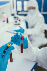 cropped view of biochemist holding test tubes with blood samples near colleague