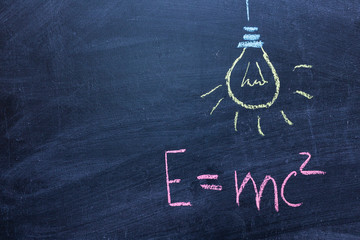 Well-known physical formula. E=mc2 on a chalk Board. Drawing of a light bulb. The concept of a...