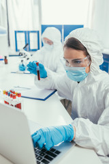Naklejka na ściany i meble biotechnologist holding test tube with blood sample and using laptop