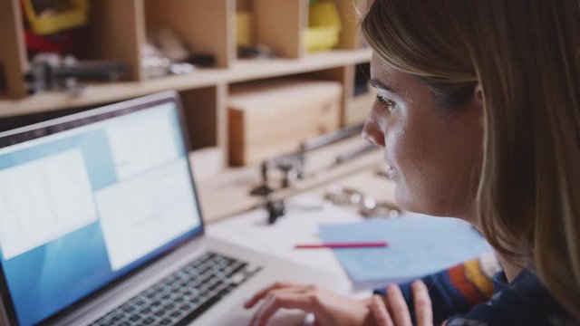 Close up of female engineer in workshop using laptop and making notes on plan for bicycle - shot in slow motion