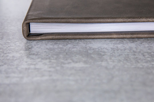 Gray grey leather bound book photo album with thick pages laying on a a light colored surface with a marbled white and gray background with lots of copy space for text with copy space