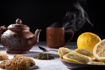 clay teapot with fresh tea and sliced ​​lemon on a dark background