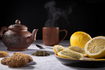 freshly brewed tea in a clay teapot with lemon, on a dark background