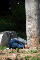 Athens, Greece, April 2020: Homeless man laying sleeping amongst ancient Greek columns