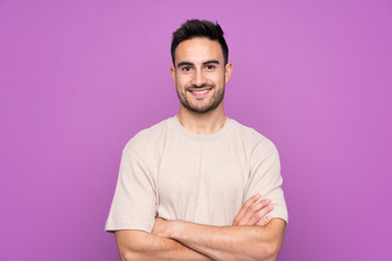 Young handsome man over isolated purple background keeping the arms crossed in frontal position